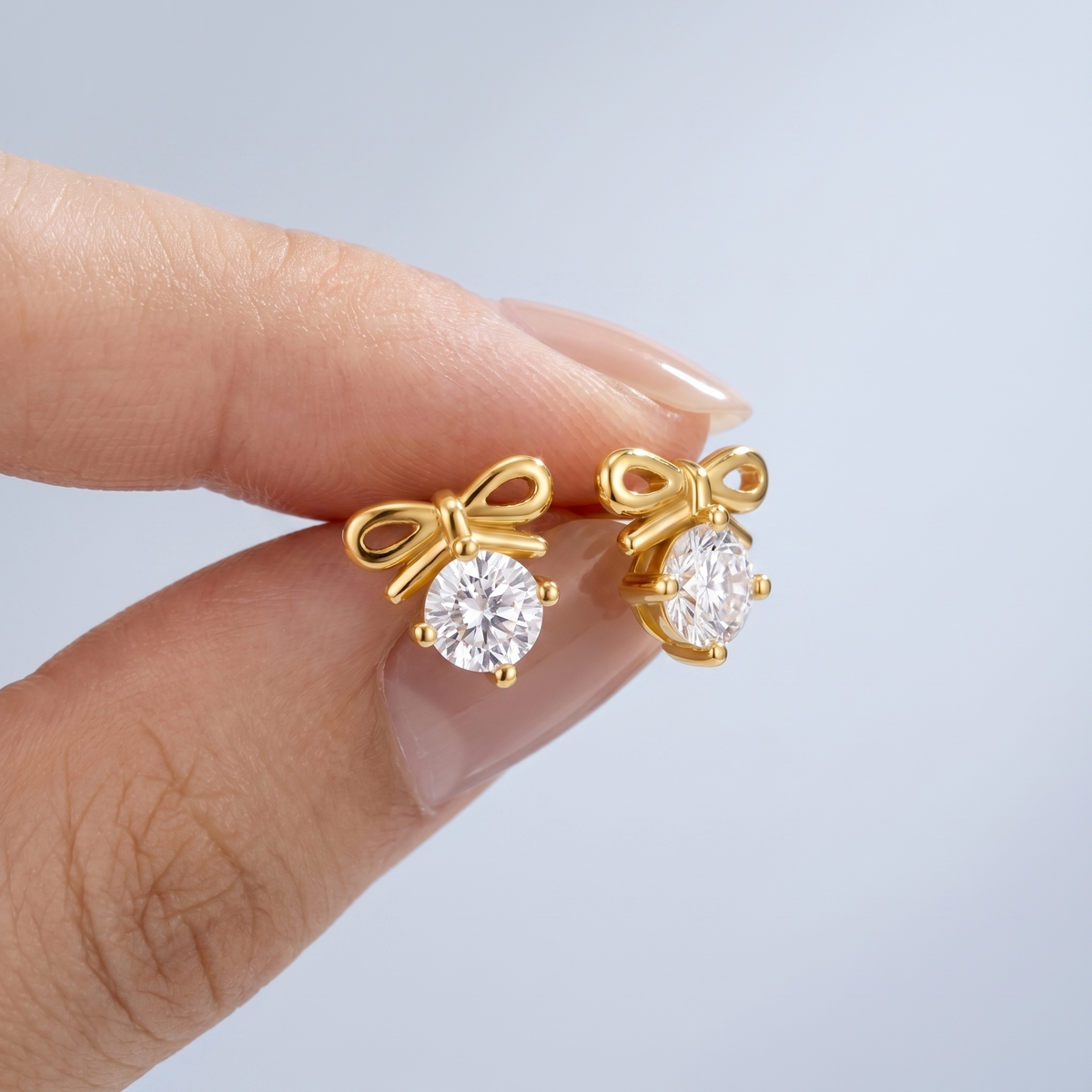 Orecchini fiocco con cristallo placcati oro 18K tenuti tra le dita, per vedere le dimensioni reali
