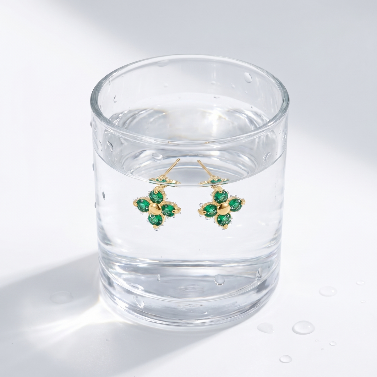 Pendientes flor verde esmeralda bañados en oro de 18K en un vaso de agua