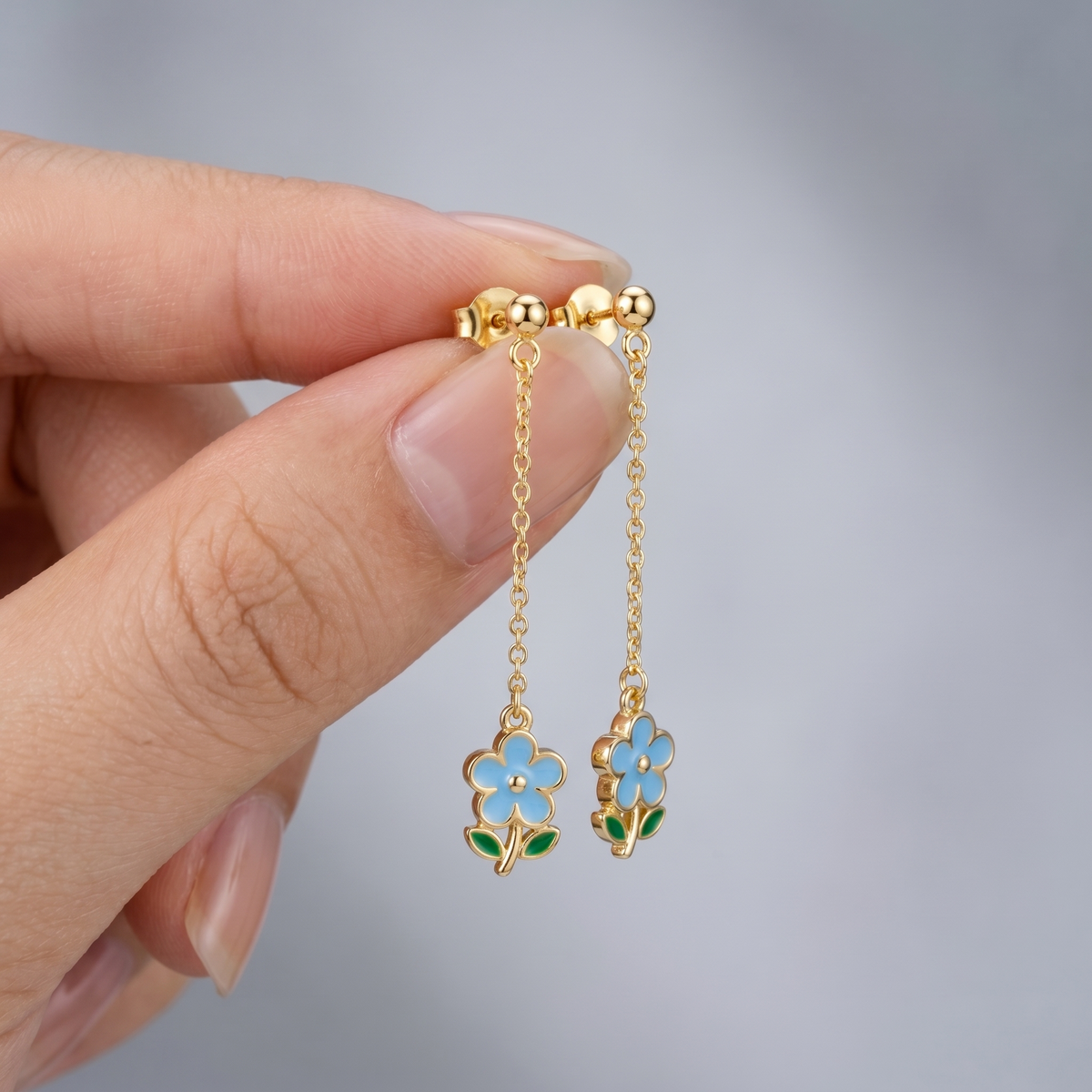 Pendientes gota con flor bañados en oro de 18K sostenidos entre los dedos, para ver el tamaño real