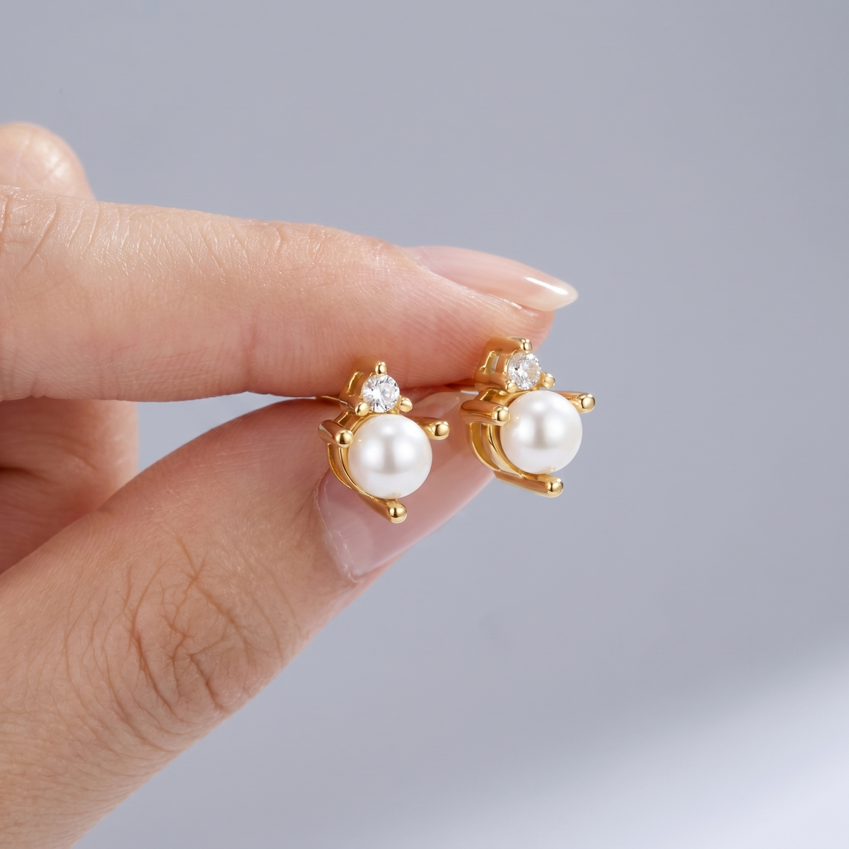 Pendientes de perla y cristal bañados en oro de 18K sostenidos entre los dedos, para ver el tamaño real